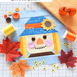 May include: A patchwork quilt block pattern for a scarecrow with a blue hat, orange hair, and a brown nose. The block is surrounded by fall-themed decorations, including orange pumpkins, yellow flowers, and red maple leaves. The pattern is called "Sweet Scarecrow" and is designed by Trellis & Thyme.