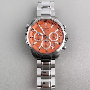 May include: A stainless steel Bulova watch with an orange face and a matching stainless steel band. The watch face features three sub-dials and the Bulova logo. The watch has a sporty design.