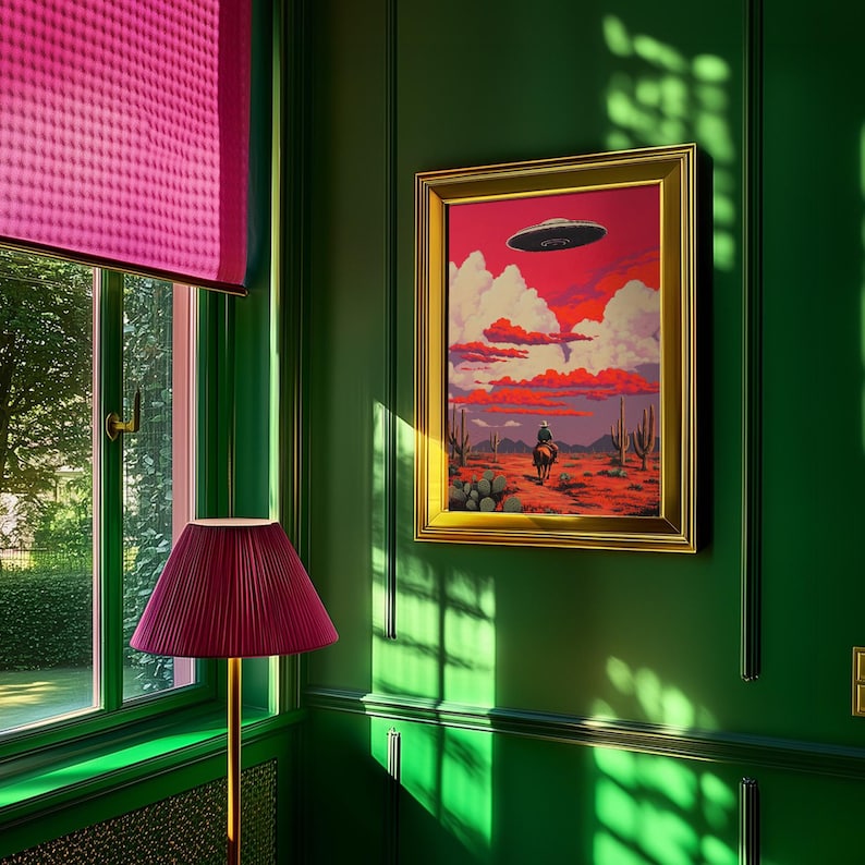 May include: A framed painting of a cowboy riding a horse in a desert landscape with a UFO flying overhead. The painting is set against a green wall with a pink lampshade in the corner.