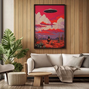 May include: A framed illustration of a cowboy riding a horse in a desert landscape with a flying saucer in the sky. The sky is a vibrant red and orange with fluffy white clouds. The desert is a sandy brown with cacti and other desert plants.