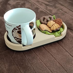 Könnte beinhalten: Eine weiße Kaffeetasse mit einem braunen und schwarzen Design, auf dem "coffee time" steht. Die Tasse steht auf einem beigefarbenen Untersetzer mit einem kleinen Teller Kekse daneben.