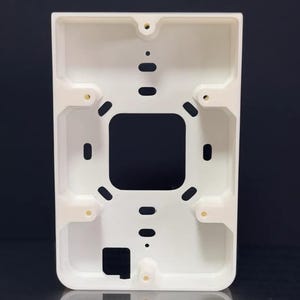 Op de afbeelding: Witte elektrische plastic doos met meerdere gaten en een vierkante opening in het midden.