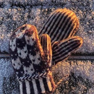 May include: A pair of knitted mittens, one with a striped pattern and the other with a geometric pattern. The mittens are a dark gray and white color.