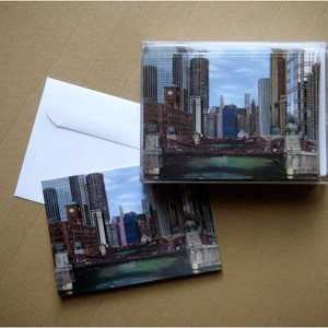 May include: A set of postcards featuring a cityscape with tall buildings and a river. The postcards are in a clear plastic sleeve.