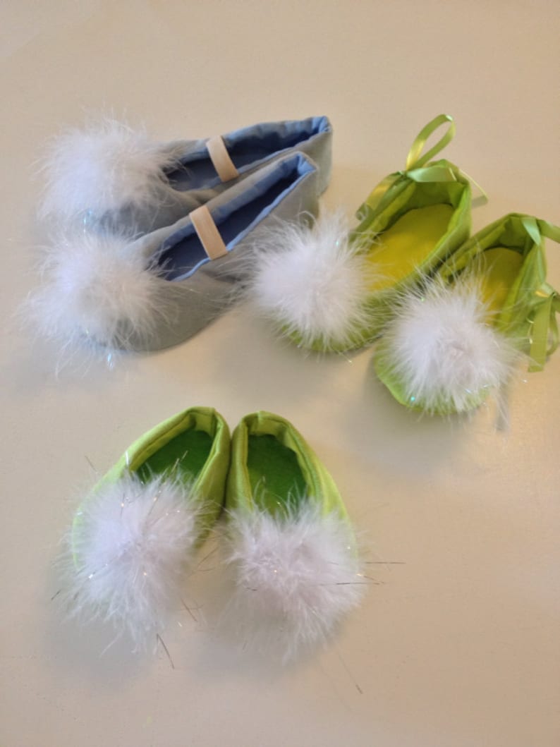 May include: Three pairs of soft slippers featuring fluffy white pom-poms on the toes. One pair is light blue with elastic straps, while the other two pairs are lime green, with one featuring green ribbon ties and the other having a simple slip-on design.