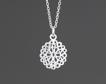 Può includere: Una collana d'argento con un delicato ciondolo circolare che presenta un design ritagliato che ricorda un fiore.