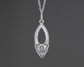 Può includere: Una collana d'argento con un delicato ciondolo ornato a forma di lacrima. Il ciondolo presenta un design a filigrana e un piccolo cuore nella parte inferiore.