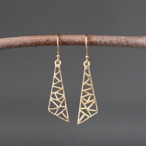 May include: A pair of gold geometric dangle earrings with a triangular shape and a delicate, intricate design.