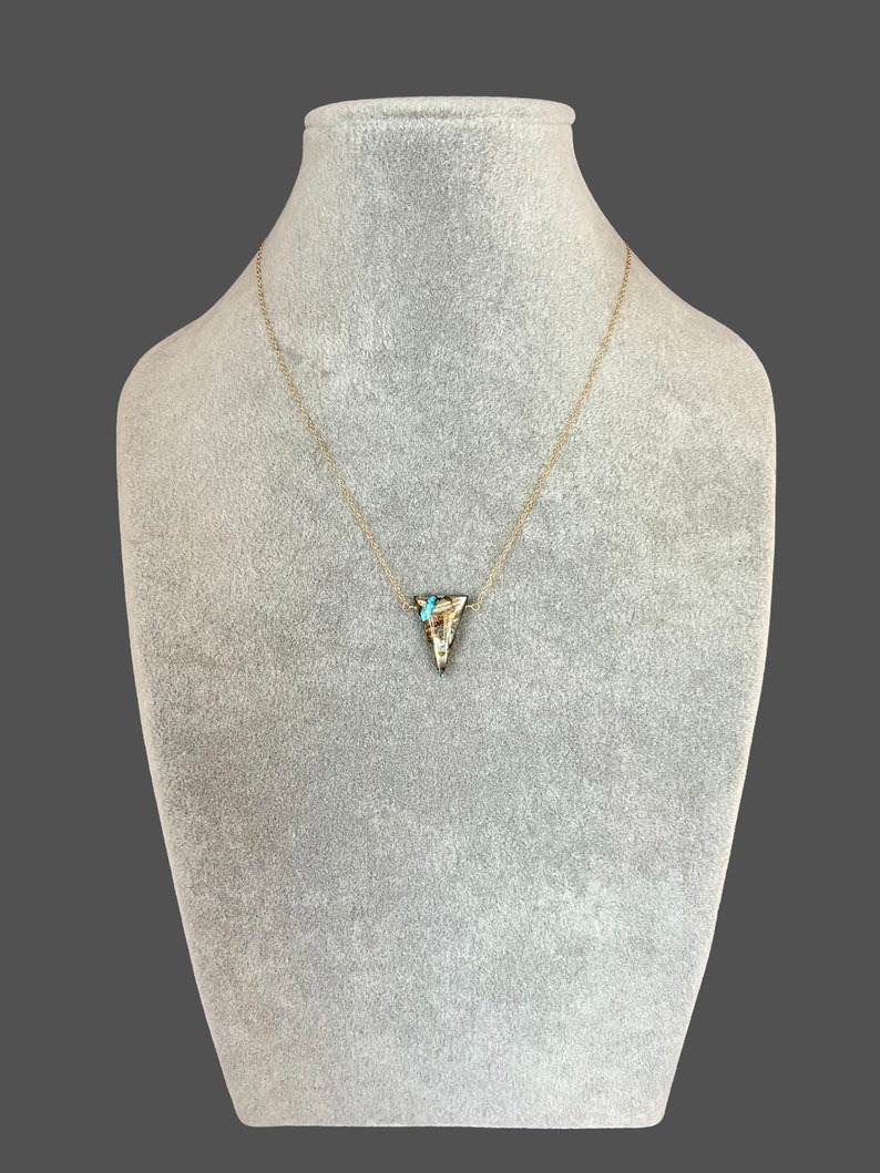 Peut inclure: Un collier en cha&icirc;ne dor&eacute;e avec un pendentif triangulaire en pierre brune, blanche et bleue.