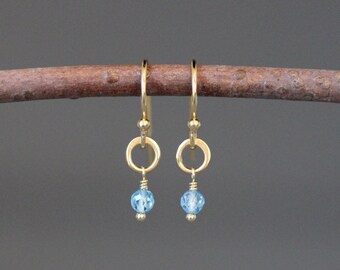 May include: Gold hoop earrings with a small blue gemstone dangling from each hoop.