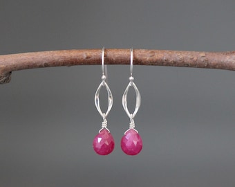 Pode incluir: Um par de brincos de prata com um design delicado e vazado e um pingente de pedra rosa. Os brincos estão pendurados em um galho.