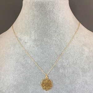 May include: A gold chain necklace with a delicate, circular pendant featuring a filigree design.