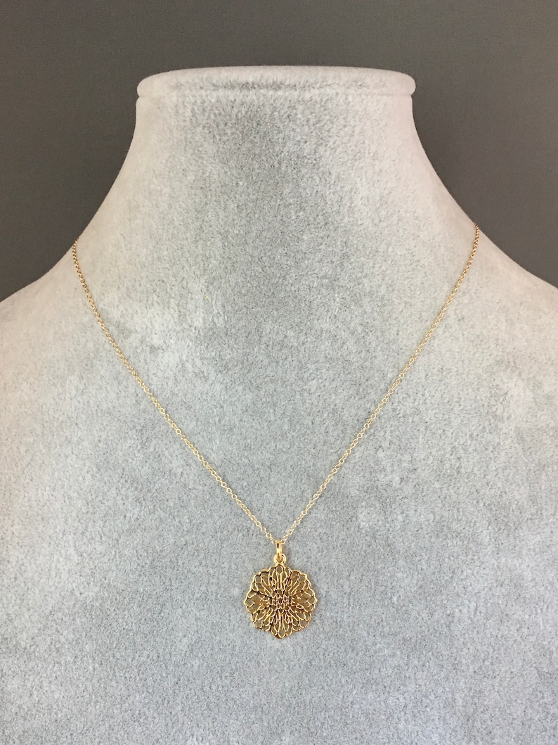 May include: A gold chain necklace with a delicate, circular pendant featuring a filigree design.