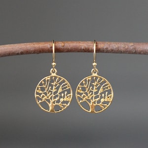 May include: Gold-toned tree of life earrings with a delicate, intricate design. The earrings are circular and feature a detailed tree silhouette.