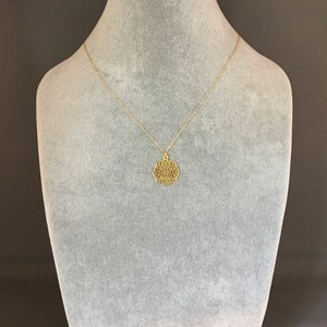 May include: A gold necklace with a delicate, intricate pendant in the shape of a mandala. The necklace is displayed on a gray velvet bust form.