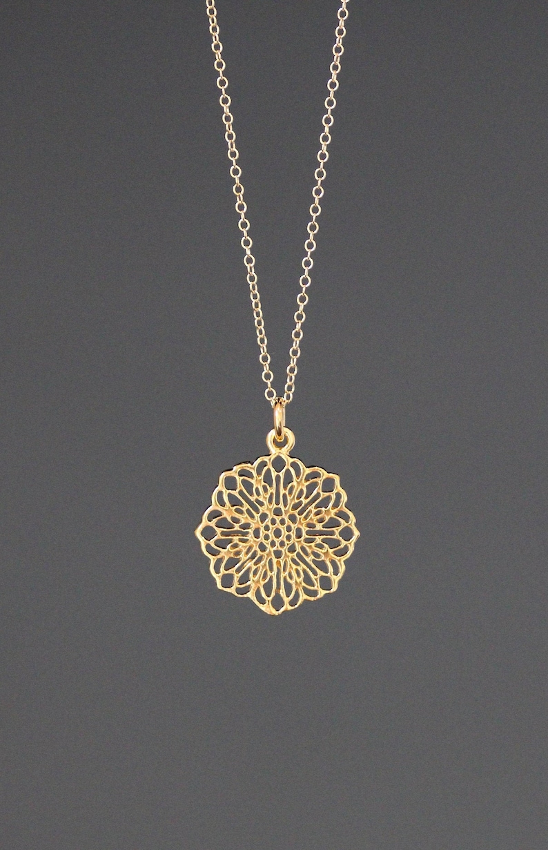 May include: A gold chain necklace with a delicate, intricate, circular pendant that resembles a flower.