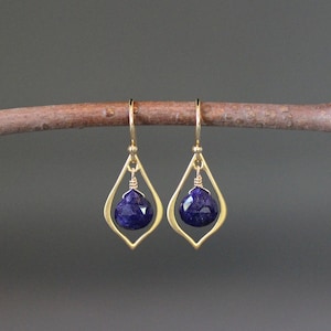 Puede incluir: Pendientes de oro con un diseño en forma de lágrima que presenta una piedra preciosa azul oscuro.