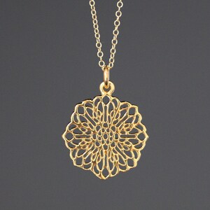 May include: A gold necklace with a delicate, intricate, circular pendant that resembles a flower.