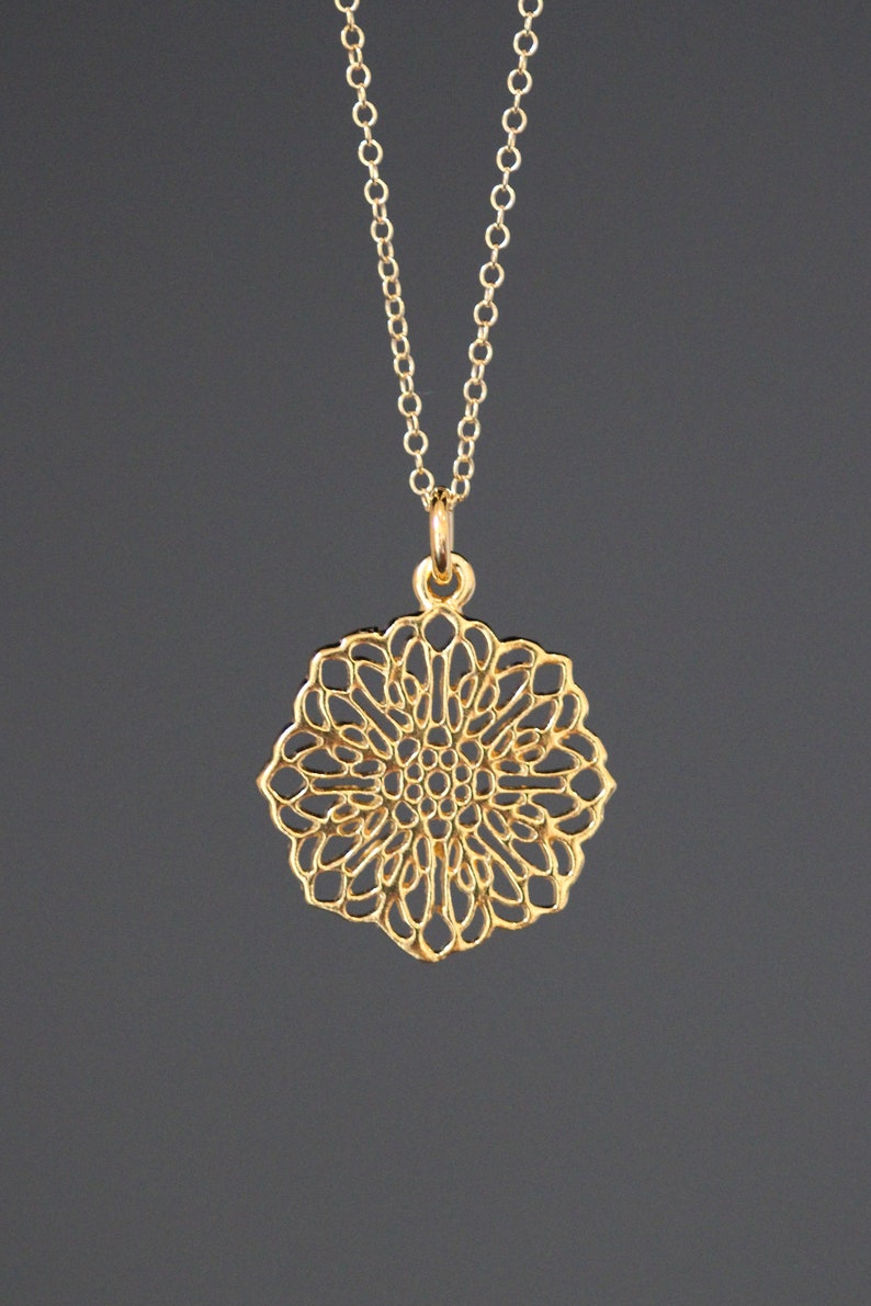May include: A gold necklace with a delicate, intricate, circular pendant that resembles a flower.