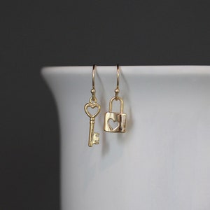 May include: A pair of gold earrings, one shaped like a key with a heart-shaped hole, and the other shaped like a padlock with a heart-shaped hole.