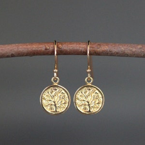 May include: Gold tree of life earrings with a delicate design. The earrings are hanging from a branch.