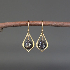 May include: Gold dangle earrings with a black gemstone in a teardrop shape.