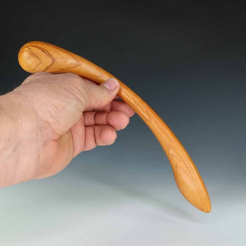 May include: A smooth, curved wooden tool with a rounded tip. The tool is made of light brown wood with a natural grain pattern.