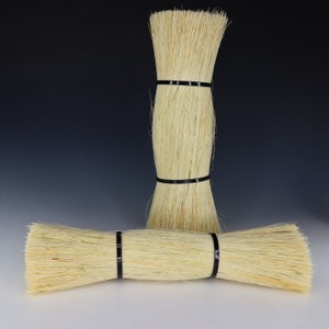 May include: Two natural fiber brushes with black elastic bands. The brushes are made of a light beige material and are bundled together.