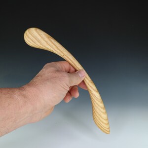 May include: A wooden spoon with a curved handle and a rounded end. The spoon is made of light wood with a natural grain pattern.