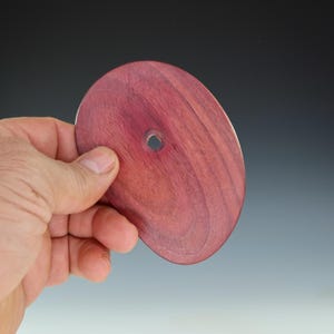May include: A round, oval-shaped piece of wood with a hole in the center. The wood is a deep reddish-purple color.