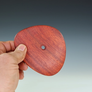 May include: A smooth, reddish-brown wooden disc with a small hole in the center. The disc is slightly oval-shaped and has a natural wood grain pattern.