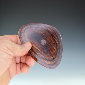 May include: A dark brown wooden disc with a hole in the center. The disc has a smooth, polished surface and a slightly irregular shape.