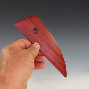 May include: A red wooden sculpting tool with a curved blade and a hole in the handle.