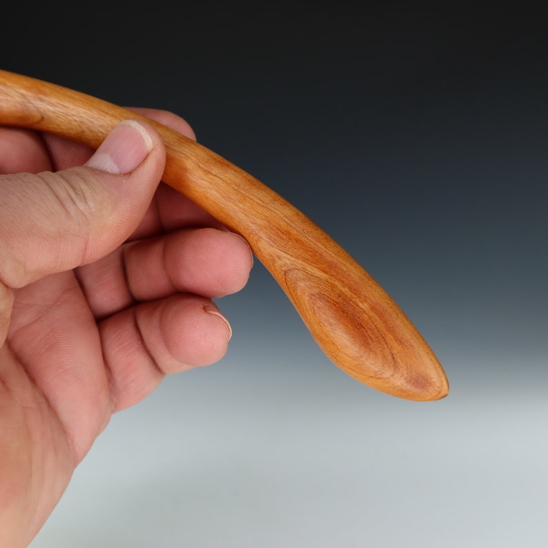 May include: A smooth, wooden spoon with a curved handle. The spoon is made of cherry wood and has a natural reddish-brown color.