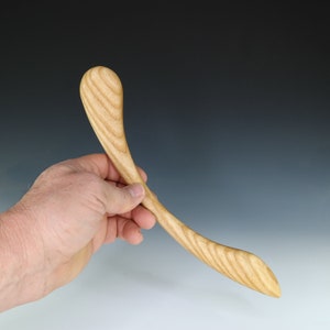 May include: A wooden spoon with a curved handle and a rounded end. The spoon is made of light-colored wood with a natural grain pattern.