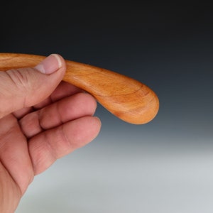 May include: A close-up of a wooden spoon with a teardrop-shaped bowl. The spoon is made of light brown wood and has a smooth, polished finish.
