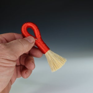 May include: A small red and white brush with a looped handle. The brush is made of natural fibers and is perfect for cleaning delicate surfaces.