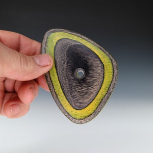 May include: A wooden, triangular-shaped pendant with a hole in the center. The pendant is black with yellow and green stripes.