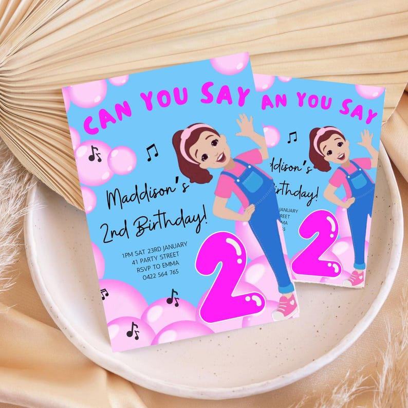 Pu&ograve; includere: Un invito di compleanno blu e rosa con una ragazza dei cartoni animati che soffia bolle. L'invito dice "Can you say" e "Maddison's 2nd Birthday!" con i dettagli per la festa.