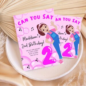 May include: Pink birthday invitation with a cartoon girl in overalls and a pink number 2. The text reads "Can You Say" and "Maddison's 2nd Birthday!" with details for the party.