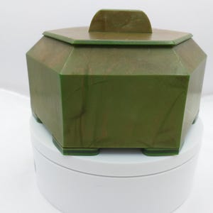 May include: A green hexagonal box with a lid. The box has a marbled pattern and is made of plastic.