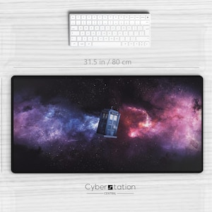 Peut inclure: Tapis de souris rectangulaire noir avec un motif de galaxie et une cabine téléphonique bleue. Le tapis mesure 80 cm sur 40 cm. Un clavier et une souris blancs sont également visibles.