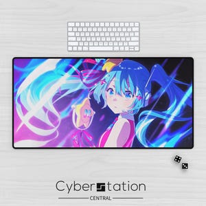 Peut inclure: Un grand tapis de bureau rectangulaire noir avec une illustration colorée de style anime d'un personnage aux cheveux bleus et une tenue rose. Le tapis porte le texte "Cyber Station CENTRAL" en bas. Un clavier blanc est au-dessus du tapis.