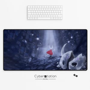 May include: A black rectangular mouse mat with a digital illustration of a character in a red cape and a white mask, set in a dark, cavernous scene. The mouse mat has the text "Cyberstation - Central" at the bottom, with a white keyboard at the top.