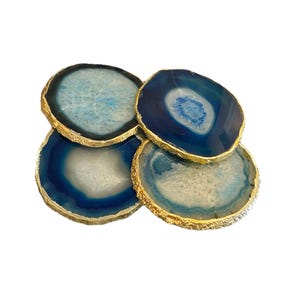 May include: Four blue agate coasters with gold gilded edges. The coasters have a natural, organic pattern with shades of blue and white. The gold edges add a touch of elegance to these decorative coasters.