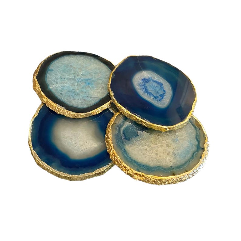 May include: Four blue agate coasters with gold gilded edges. The coasters have a natural, organic pattern with shades of blue and white. The gold edges add a touch of elegance to these decorative coasters.