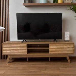 May include: A light brown wooden TV stand with a mid-century modern design. The stand has two sliding doors with horizontal grooves and a central open shelf. A large black television sits on top.