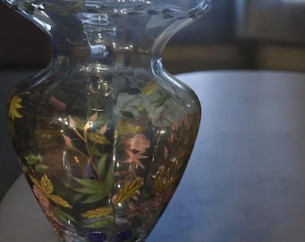 May include: A clear glass vase with a floral design. The vase has a wide mouth and a narrow base. The flowers are painted in shades of pink, yellow, green, and blue.