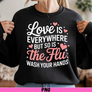 May include: Black sweatshirt with the text "Love is everywhere but so is the Flu, wash your hands" in white and pink. The design includes pink hearts and stars. The sweatshirt has long sleeves.