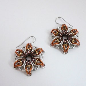 May include: A pair of handmade flower-shaped earrings. The earrings are made of silver-colored metal rings, with accents of copper, bronze, and gold-colored rings. The earrings have a hook closure.
